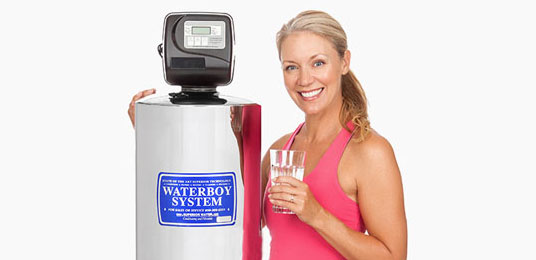 waterboy-whole-home-water-filtration-system A woman standing next to the Waterboy whole-home water filtration system with a glass of water
